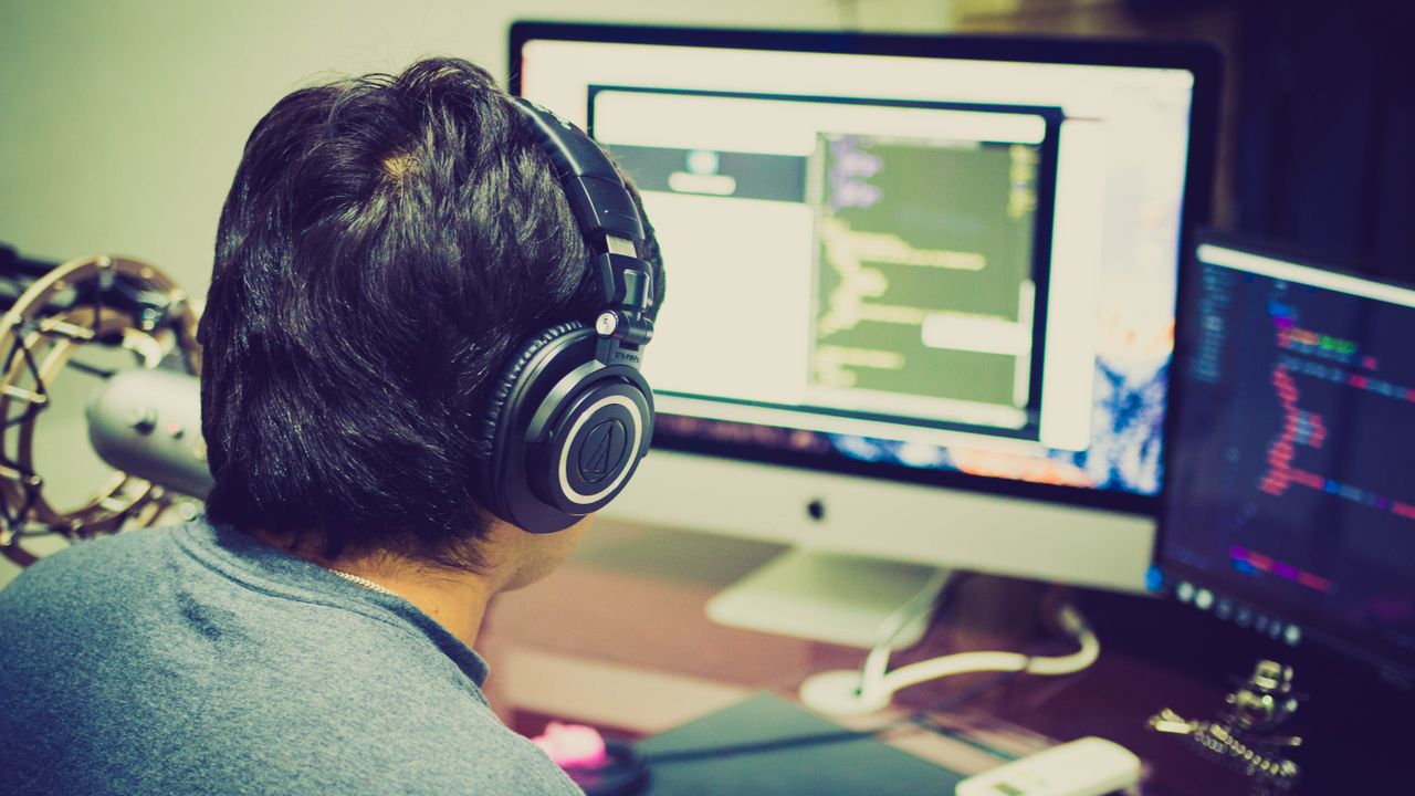 A programmer working on code with dual monitors and a laptop in a dimly lit room.