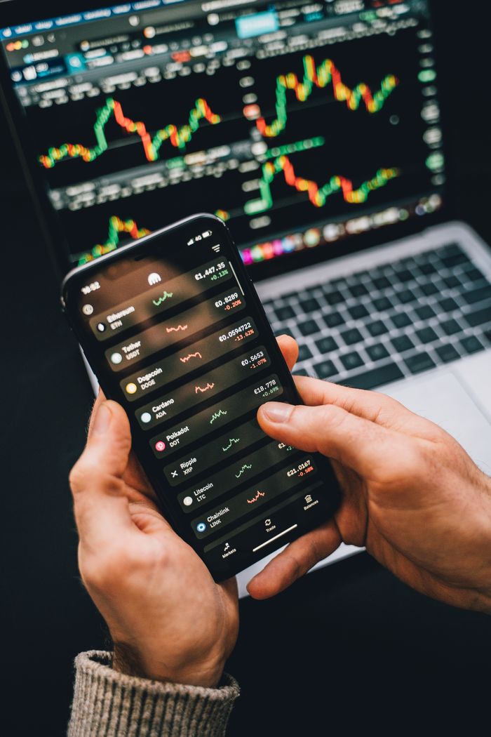 Crafting Captivating Headlines: Your awesome post title goes here Hands holding smartphone with stock app, laptop displaying charts. Perfect for financial and technology themes.