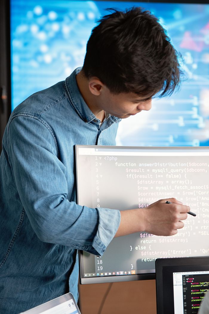 Services Asian male programmer writing code on a computer monitor in an office setting.