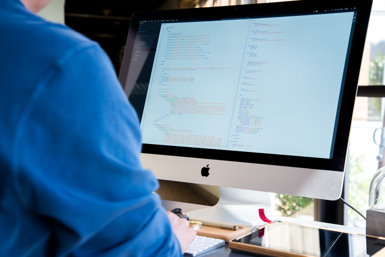 Woman programming at desk with multiple monitors in a modern office setting.